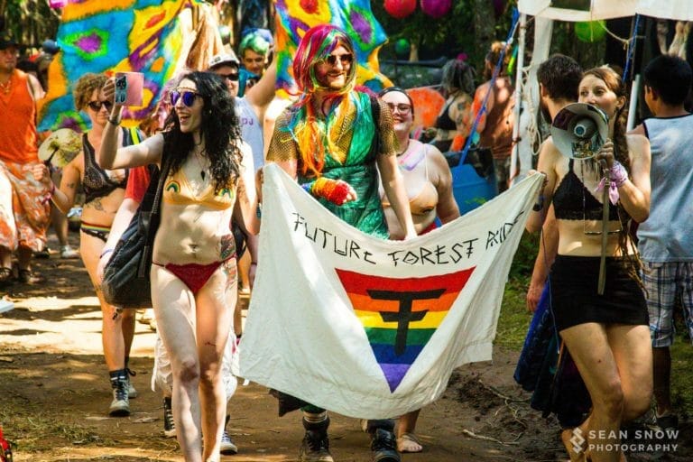 Défilé de la fierté en forêt, avec perruques arc-en-ciel, mégaphone et bannière Future Forest Pride à triangle arc-en-ciel