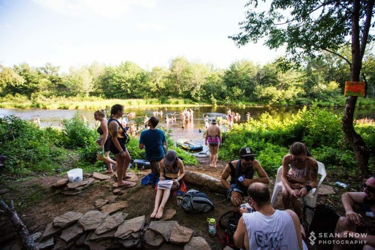 Des festivaliers se détendent sur une rive bordée de pierres pendant que d'autres se baignent dans l'eau ensoleillée
