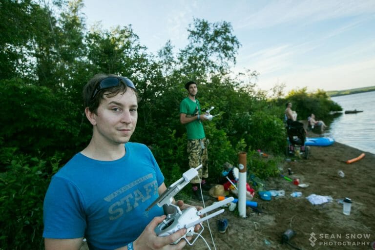 Membre de l'équipe en t-shirt Future Forest tenant une télécommande de drone au bord du lac, un autre pilote derrière