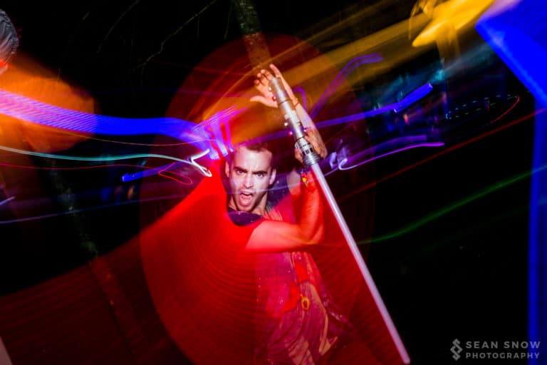 Une personne brandit un sabre laser jouet en criant, entourée de traînées de lumière rouges, bleues et orangées
