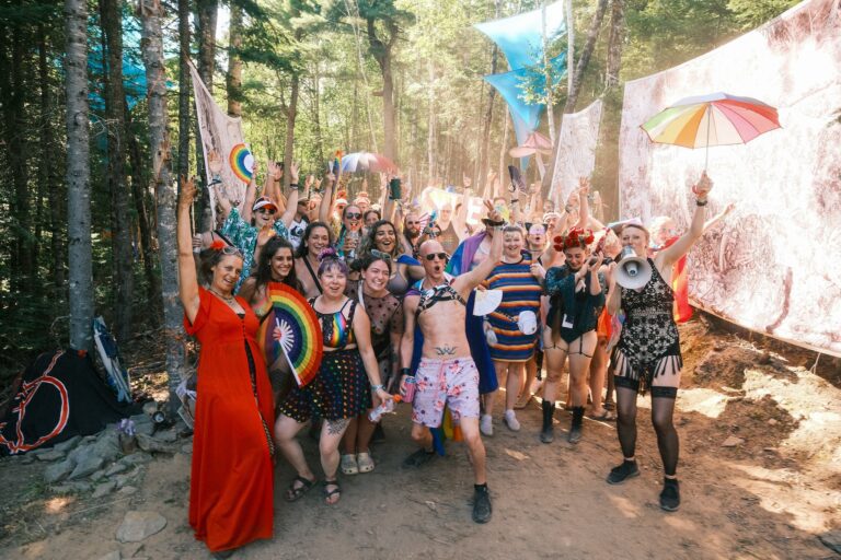 Foule costumée qui pose bras levés avec éventails et parapluie arc-en-ciel sur un sentier forestier ensoleillé