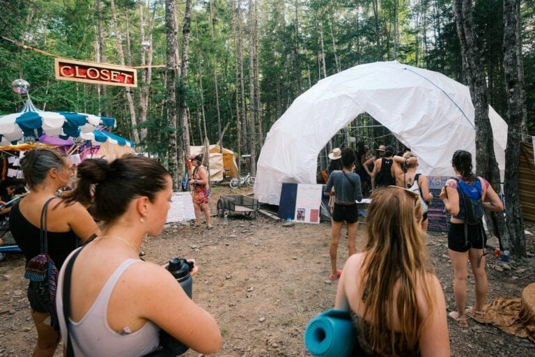 Des festivaliers avec leur tapis de yoga se rassemblent devant un dôme géodésique blanc dans une clairière