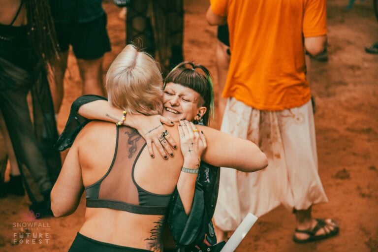 Deux festivaliers qui s'enlacent en souriant sur une aire de danse de terre rouge poussiéreuse, entourés d'autres personnes