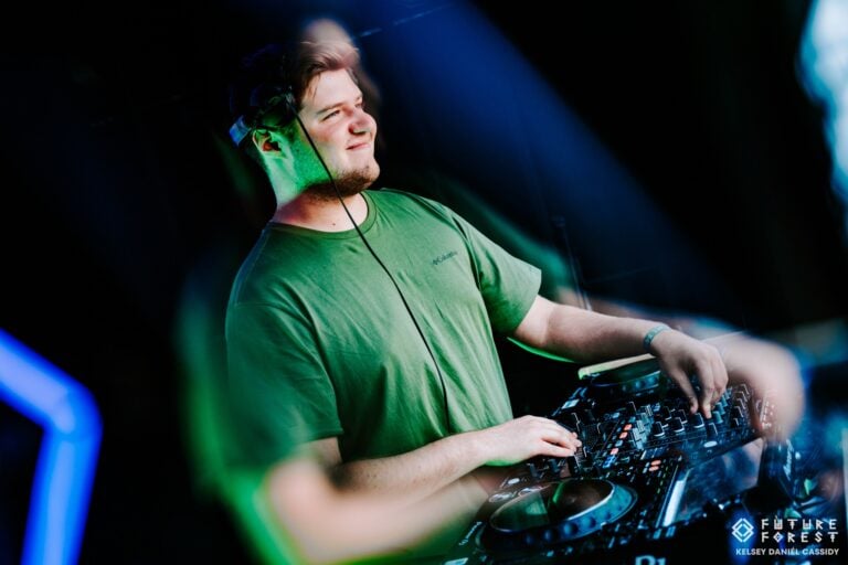 Un DJ souriant en t-shirt vert, casque sur la tête, aux commandes de la table de mixage sous un éclairage vert et bleu