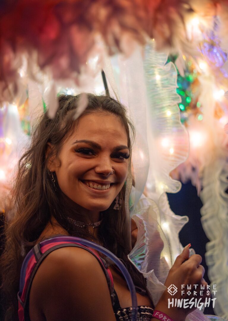 Festivalier souriant avec une bretelle de sac d'hydratation, devant un tissu blanc à volants et des lumières scintillantes