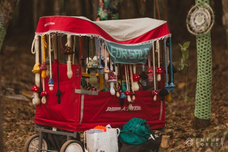 Chariot rouge à auvent garni de champignons au crochet et d'une pancarte FOR SALE, près d'un tronc d'arbre recouvert de crochet
