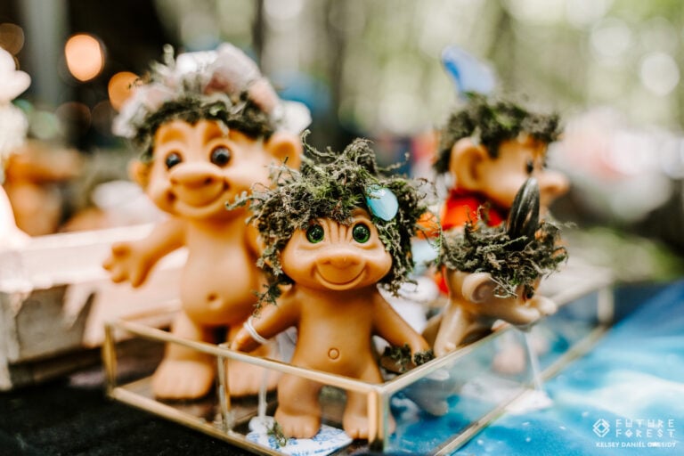 Poupées trolls aux cheveux de mousse, l'une coiffée de fleurs, dans une petite vitrine de verre posée sur une table
