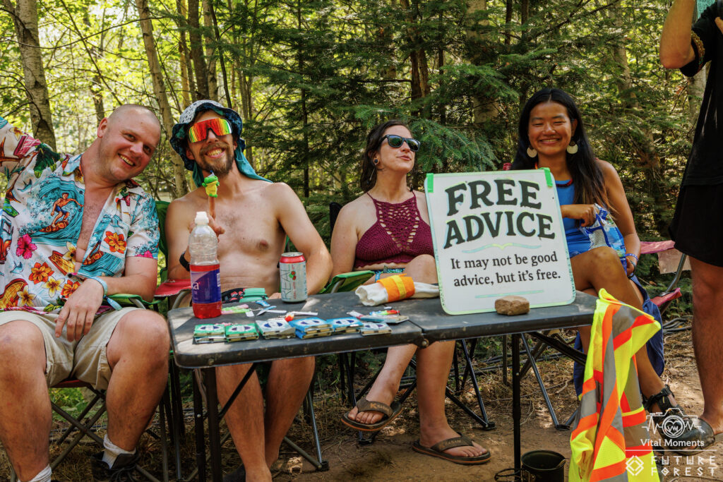 Four friends laughing at a Free Advice table among the trees in colorful outfits