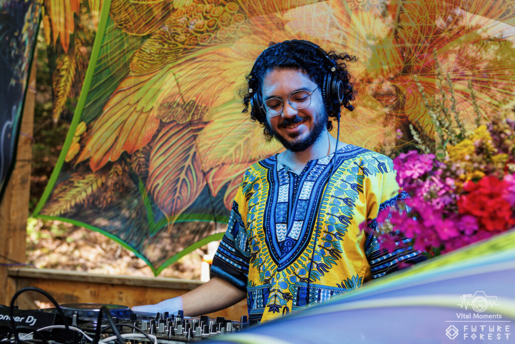 Smiling festivalgoer in a yellow patterned dashiki and headphones against vivid floral artwork