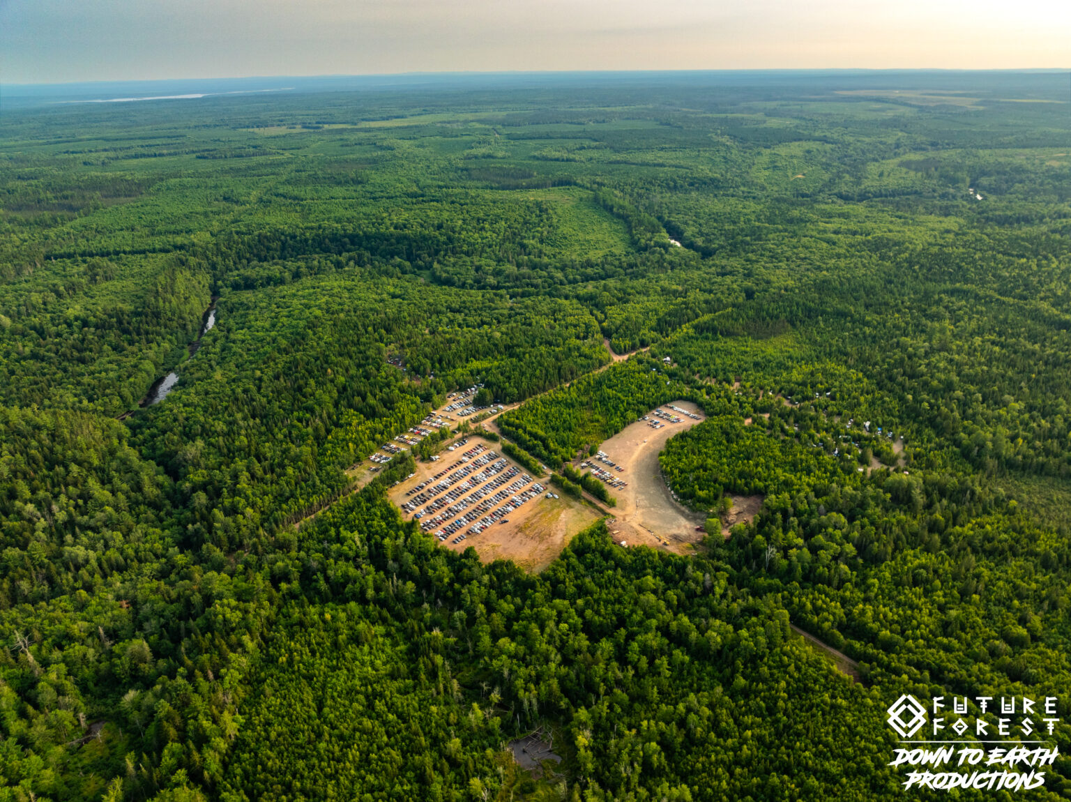 Aerial view of Future Forest grounds clearing ringed by green forest with a distant lake