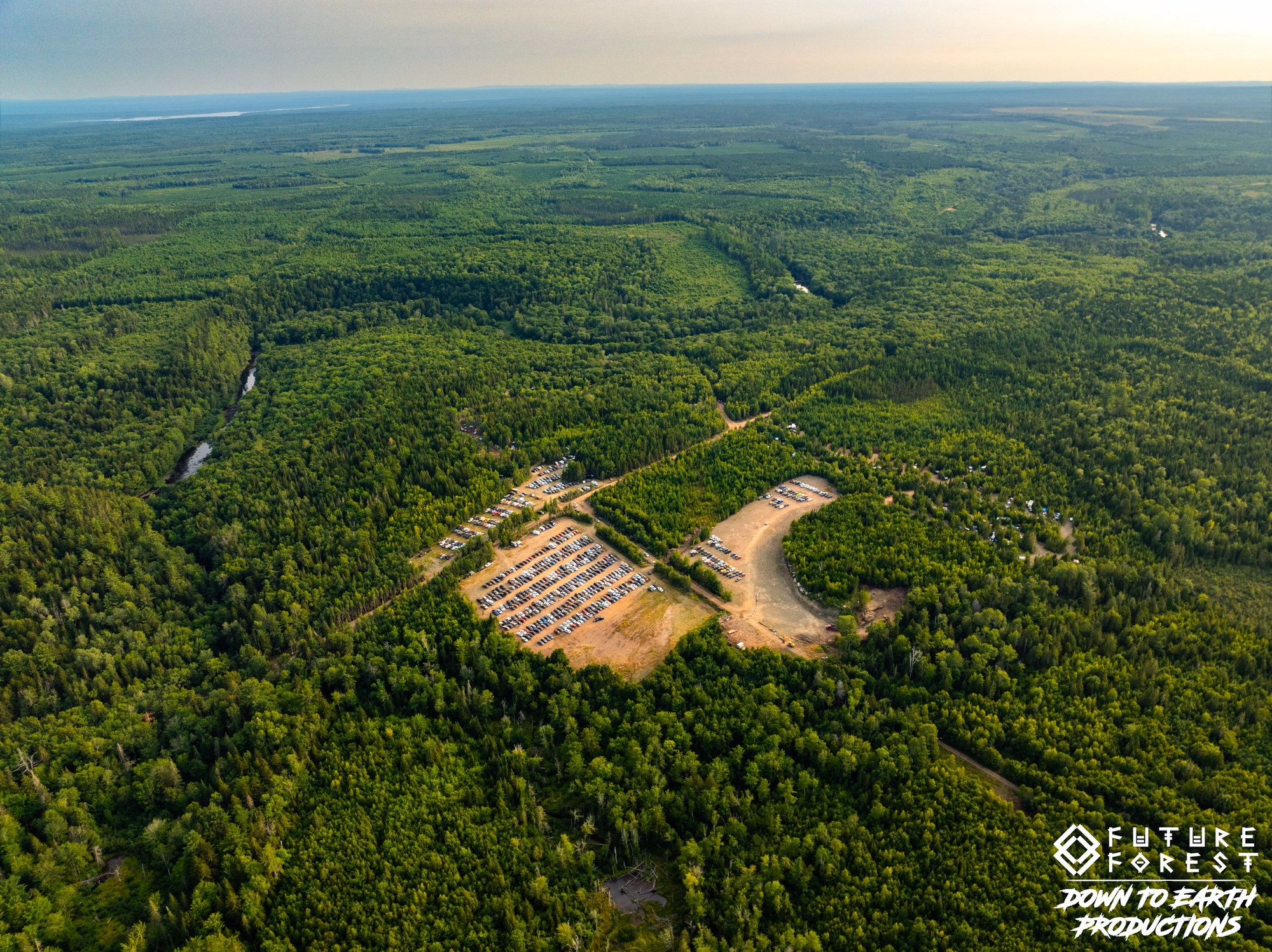 Aerial view of Future Forest grounds clearing ringed by green forest with a distant lake